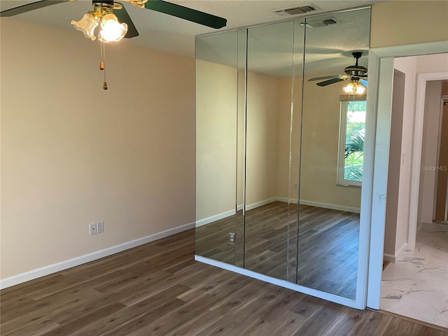 unfurnished bedroom featuring a closet, a ceiling fan, visible vents, baseboards, and wood finished floors