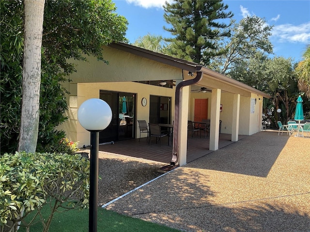 rear view of property with outdoor dining space, a ceiling fan, a patio area, and stucco siding