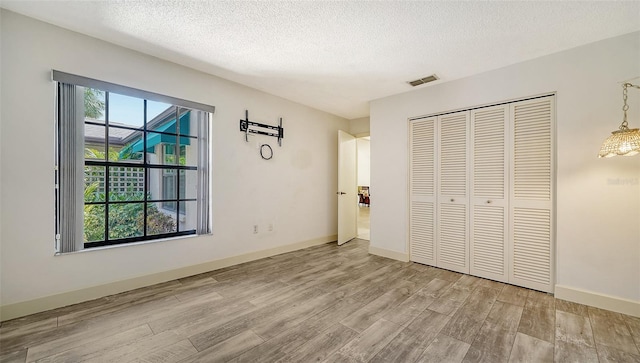 unfurnished bedroom with light wood-type flooring, a textured ceiling, and a closet