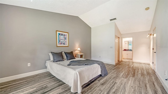 bedroom with light wood-type flooring, ensuite bath, and vaulted ceiling