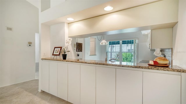 kitchen with white cabinets, decorative light fixtures, kitchen peninsula, and stone countertops