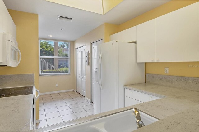 kitchen with white appliances, white cabinetry, and light tile patterned flooring