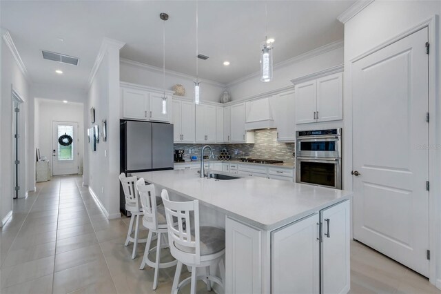 kitchen with pendant lighting, a kitchen island with sink, sink, white cabinetry, and appliances with stainless steel finishes