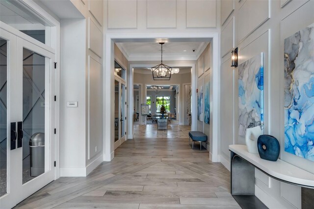 entryway with ornamental molding, light hardwood / wood-style floors, a notable chandelier, and french doors