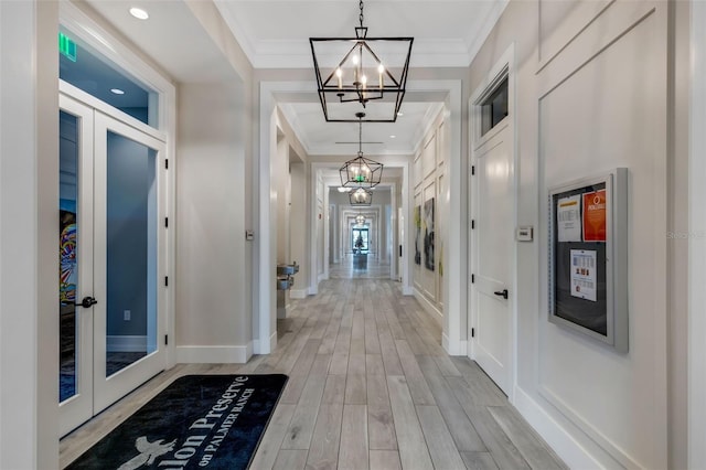 hallway with french doors, ornamental molding, an inviting chandelier, and light hardwood / wood-style floors