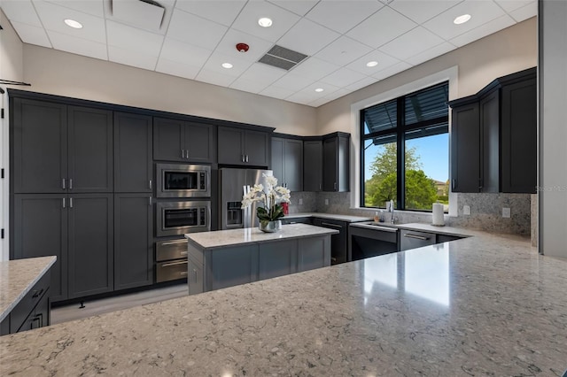 kitchen with sink, backsplash, a paneled ceiling, stainless steel appliances, and light stone countertops