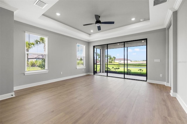 unfurnished room with ornamental molding, a wealth of natural light, light wood-type flooring, and a tray ceiling