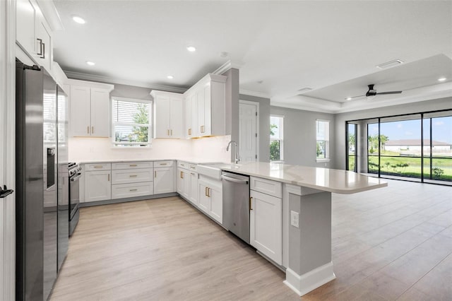 kitchen featuring sink, light wood-type flooring, kitchen peninsula, stainless steel appliances, and white cabinets