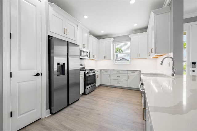 kitchen with appliances with stainless steel finishes, white cabinetry, sink, backsplash, and light hardwood / wood-style flooring