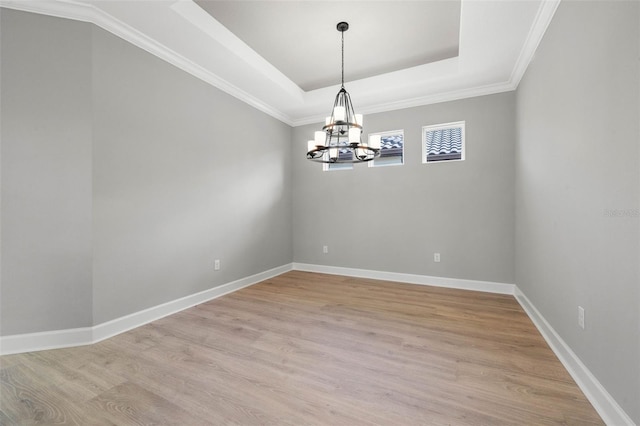 empty room with a raised ceiling, a chandelier, and light wood-type flooring