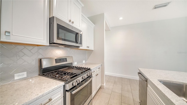 kitchen with white cabinetry, decorative backsplash, visible vents, stainless steel appliances, and light stone countertops
