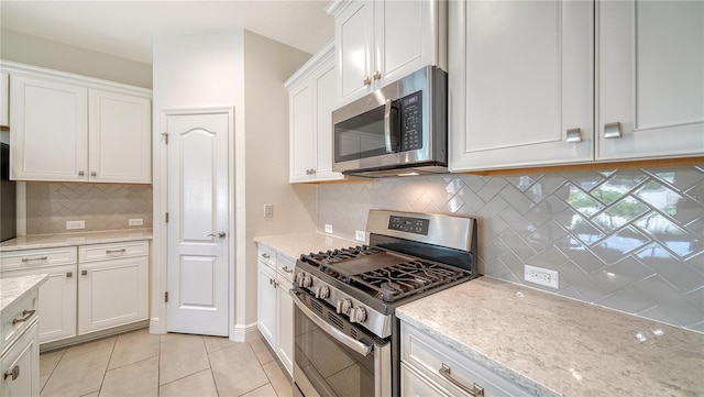 kitchen with tasteful backsplash, light stone countertops, stainless steel appliances, white cabinetry, and light tile patterned flooring