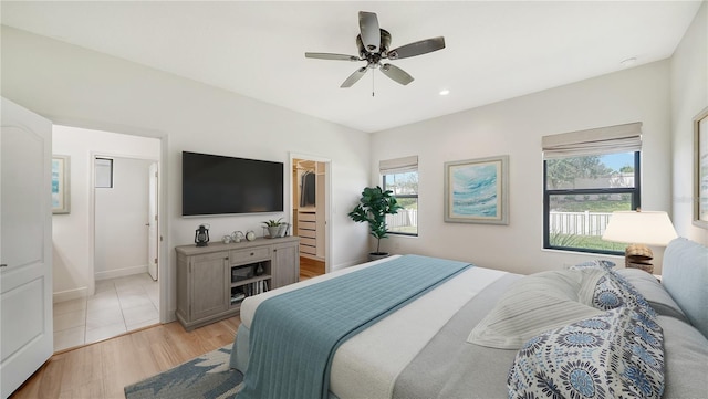 bedroom featuring ceiling fan, baseboards, light wood-type flooring, recessed lighting, and a walk in closet