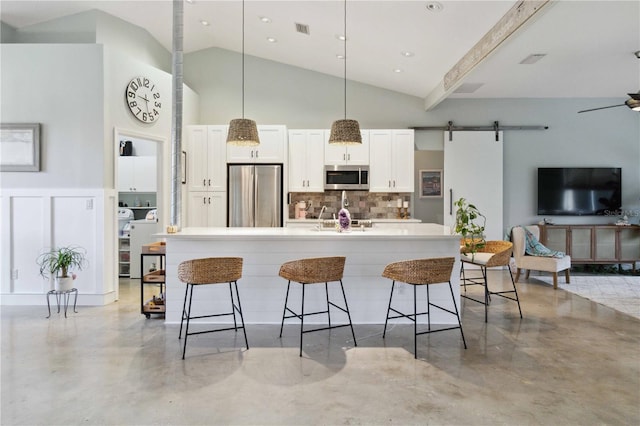 kitchen with appliances with stainless steel finishes, a kitchen breakfast bar, white cabinets, a barn door, and a kitchen island with sink