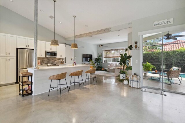 kitchen featuring appliances with stainless steel finishes, white cabinetry, backsplash, a kitchen bar, and decorative light fixtures