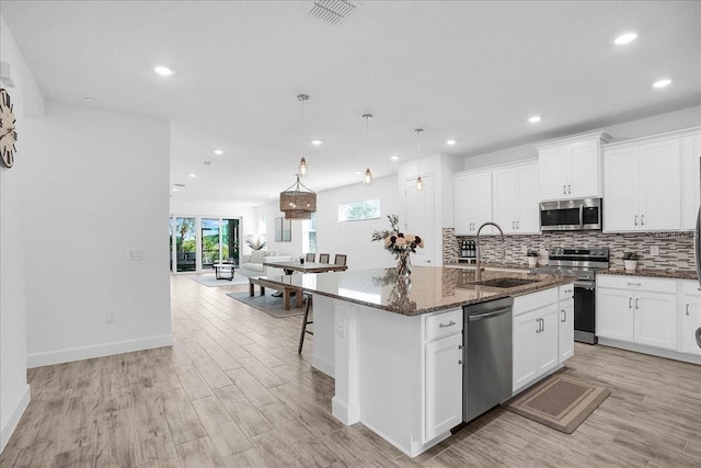 kitchen featuring decorative backsplash, an island with sink, dark stone counters, a sink, and appliances with stainless steel finishes