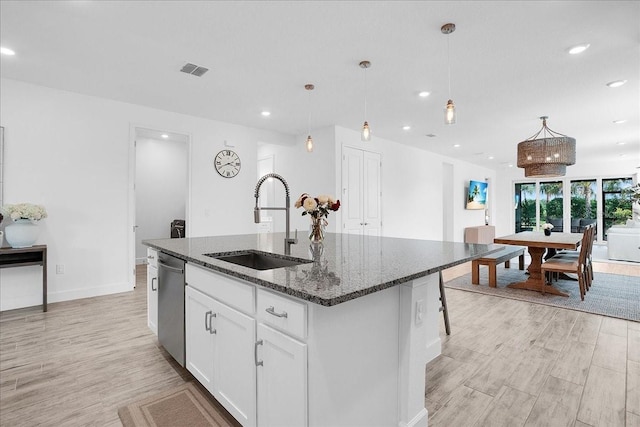 kitchen with stainless steel dishwasher, visible vents, an island with sink, a sink, and light wood-style flooring