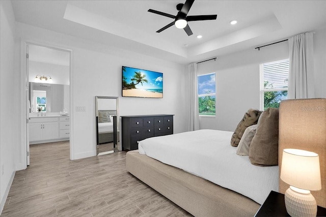 bedroom featuring baseboards, connected bathroom, light wood-style floors, a tray ceiling, and recessed lighting
