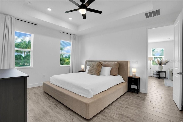 bedroom with recessed lighting, a tray ceiling, visible vents, and light wood-style floors