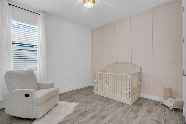 bedroom featuring baseboards, a crib, and light wood-style floors