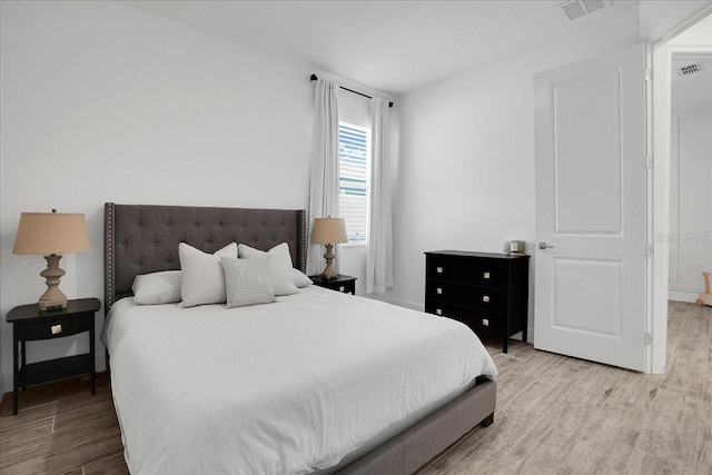 bedroom with baseboards, visible vents, and wood finished floors