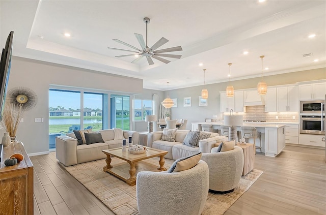 living room with ceiling fan, ornamental molding, light hardwood / wood-style flooring, and a raised ceiling