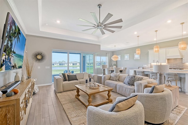 living room featuring ceiling fan, a tray ceiling, crown molding, light hardwood / wood-style floors, and a water view