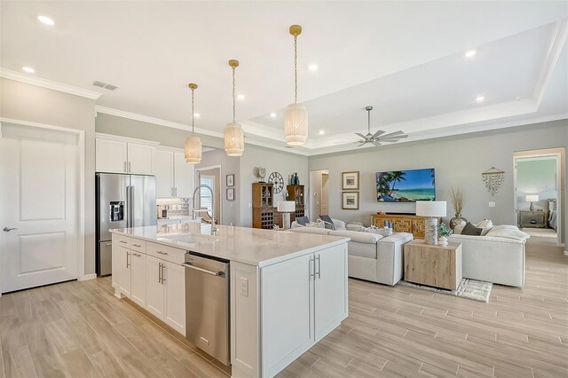 kitchen with ceiling fan, appliances with stainless steel finishes, a kitchen island with sink, and white cabinetry