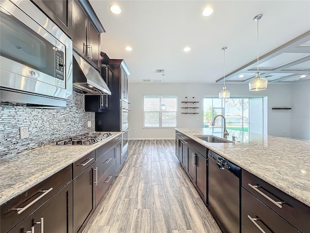 kitchen with dark brown cabinetry, sink, hanging light fixtures, stainless steel appliances, and light stone counters