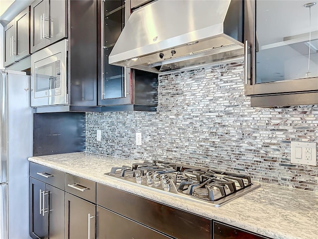 kitchen featuring backsplash, light stone counters, dark brown cabinets, ventilation hood, and stainless steel appliances