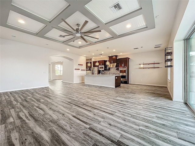 unfurnished living room featuring wood-type flooring, ceiling fan, coffered ceiling, and beam ceiling