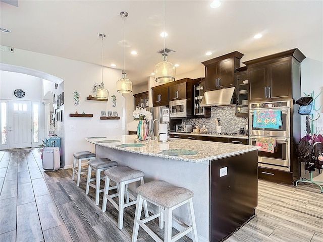 kitchen featuring a breakfast bar, dark brown cabinetry, stainless steel appliances, a kitchen island with sink, and pendant lighting