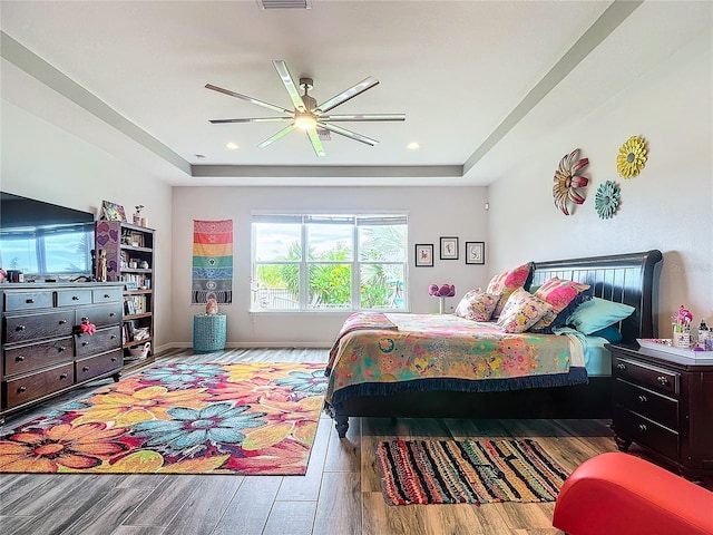 bedroom with a tray ceiling, ceiling fan, and light hardwood / wood-style flooring