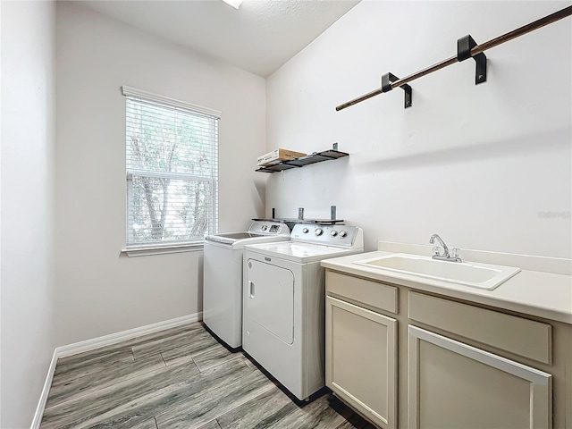 clothes washing area with cabinets, washing machine and dryer, light hardwood / wood-style flooring, and sink