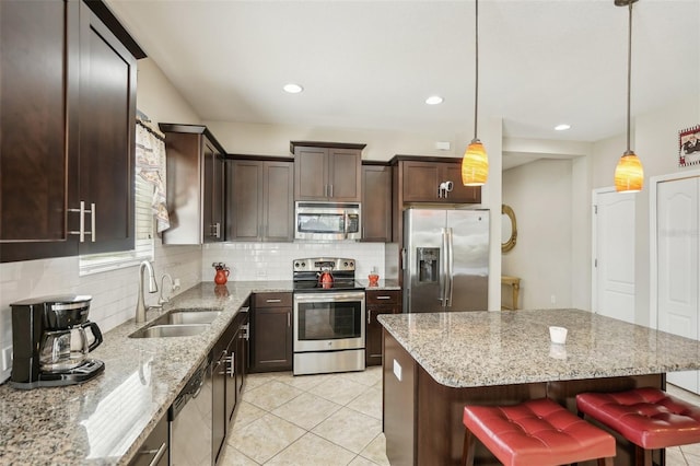 kitchen with a breakfast bar, sink, stainless steel appliances, decorative light fixtures, and light stone countertops