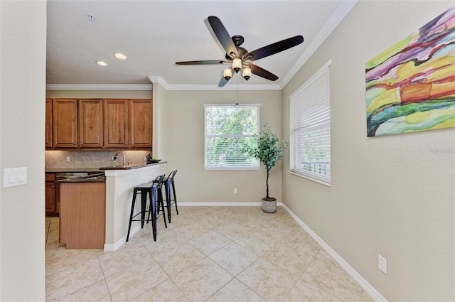 kitchen with light tile patterned flooring, backsplash, crown molding, a kitchen bar, and ceiling fan