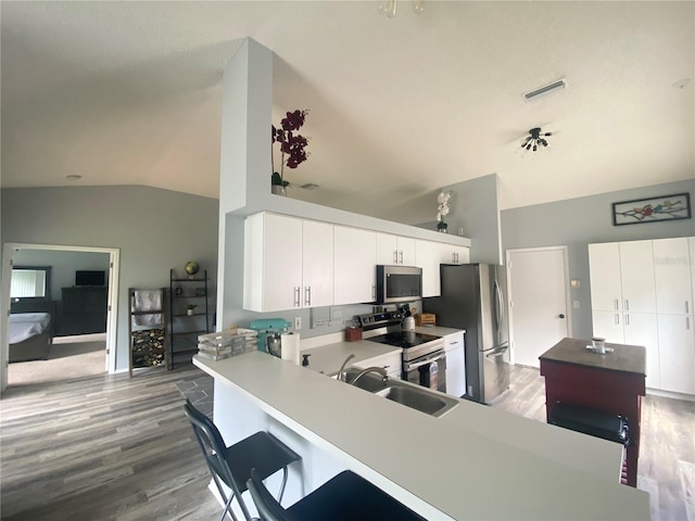 kitchen with kitchen peninsula, white cabinetry, stainless steel appliances, and lofted ceiling