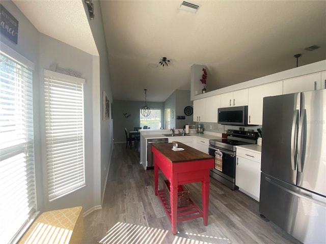 kitchen featuring white cabinets, appliances with stainless steel finishes, decorative light fixtures, and a wealth of natural light