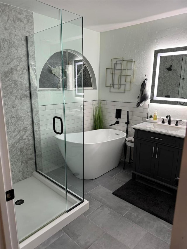 bathroom featuring tile patterned floors, vanity, tile walls, and shower with separate bathtub