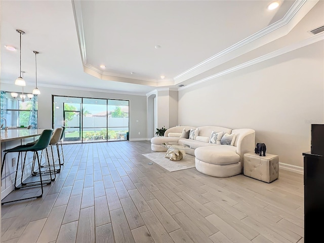 living room featuring ornamental molding, light wood-type flooring, a notable chandelier, and a raised ceiling