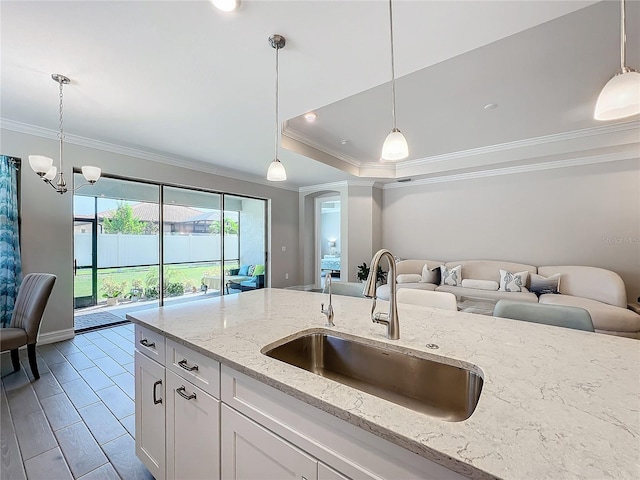 kitchen with sink, white cabinetry, hanging light fixtures, an inviting chandelier, and light stone countertops