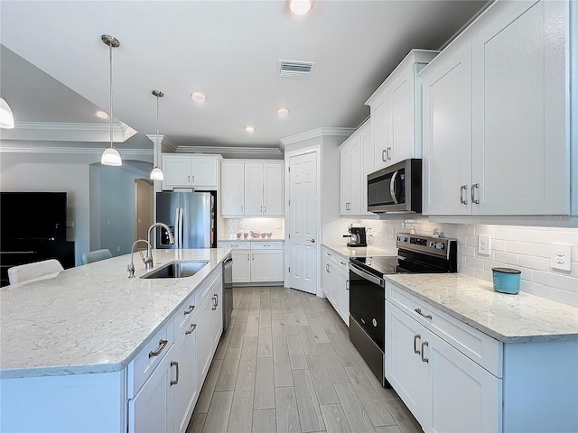 kitchen with appliances with stainless steel finishes, white cabinetry, decorative light fixtures, a kitchen island with sink, and sink