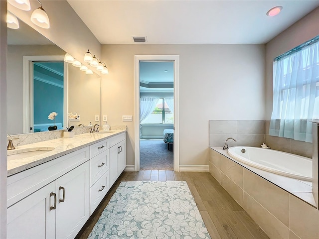 bathroom with a wealth of natural light, vanity, a relaxing tiled tub, and hardwood / wood-style flooring