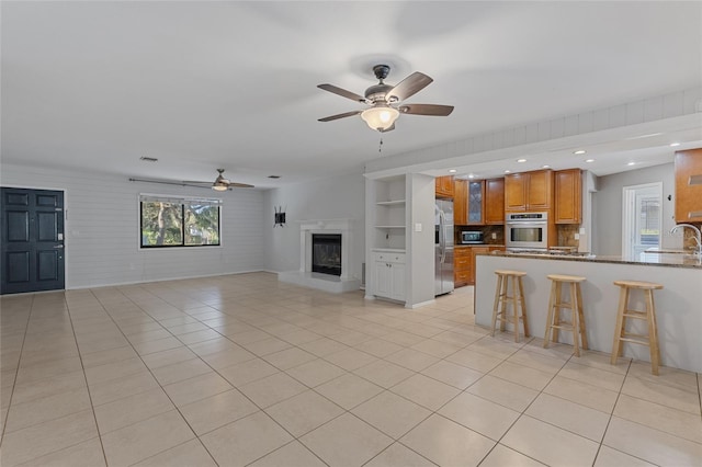 unfurnished living room featuring light tile patterned floors, sink, and ceiling fan