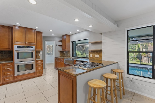 kitchen featuring appliances with stainless steel finishes, decorative backsplash, dark stone countertops, and light tile patterned floors