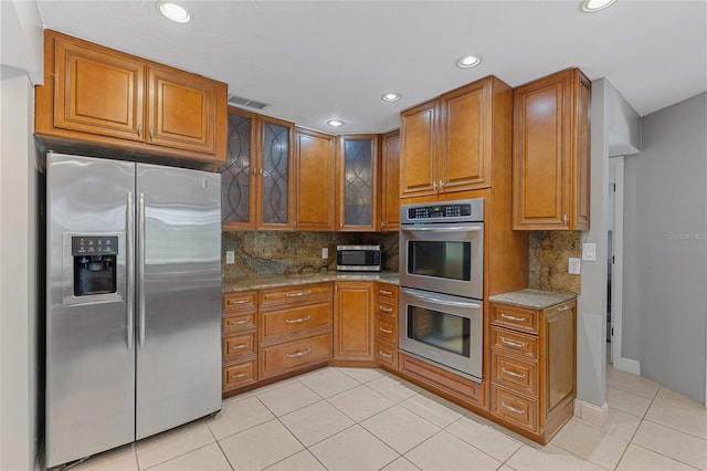 kitchen featuring light stone countertops, appliances with stainless steel finishes, backsplash, and light tile patterned floors