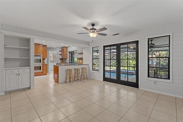 unfurnished living room featuring wood walls, light tile patterned floors, ceiling fan, french doors, and built in shelves