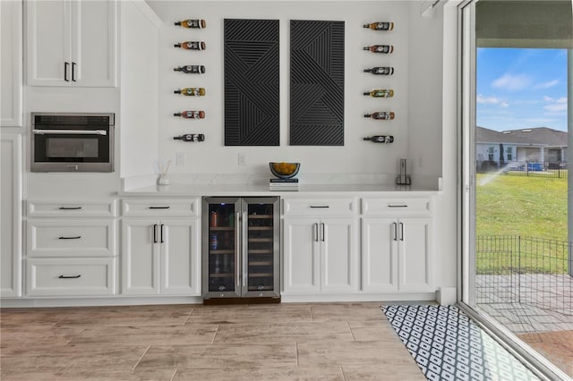 bar featuring white cabinets, wine cooler, light wood-type flooring, and stainless steel oven