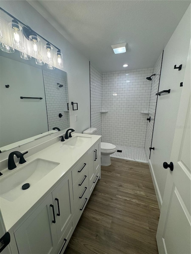 bathroom featuring tiled shower, vanity, a textured ceiling, toilet, and hardwood / wood-style floors