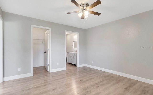 unfurnished bedroom with connected bathroom, a spacious closet, ceiling fan, and light hardwood / wood-style flooring